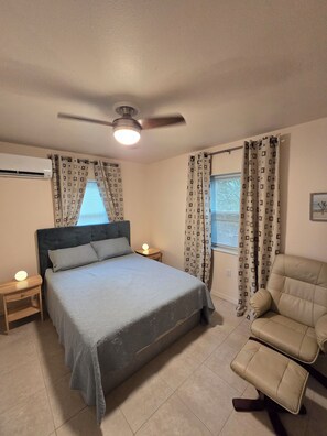A bedroom with a bed, a chair, a bedside table with a lamp, and a ceiling fan.