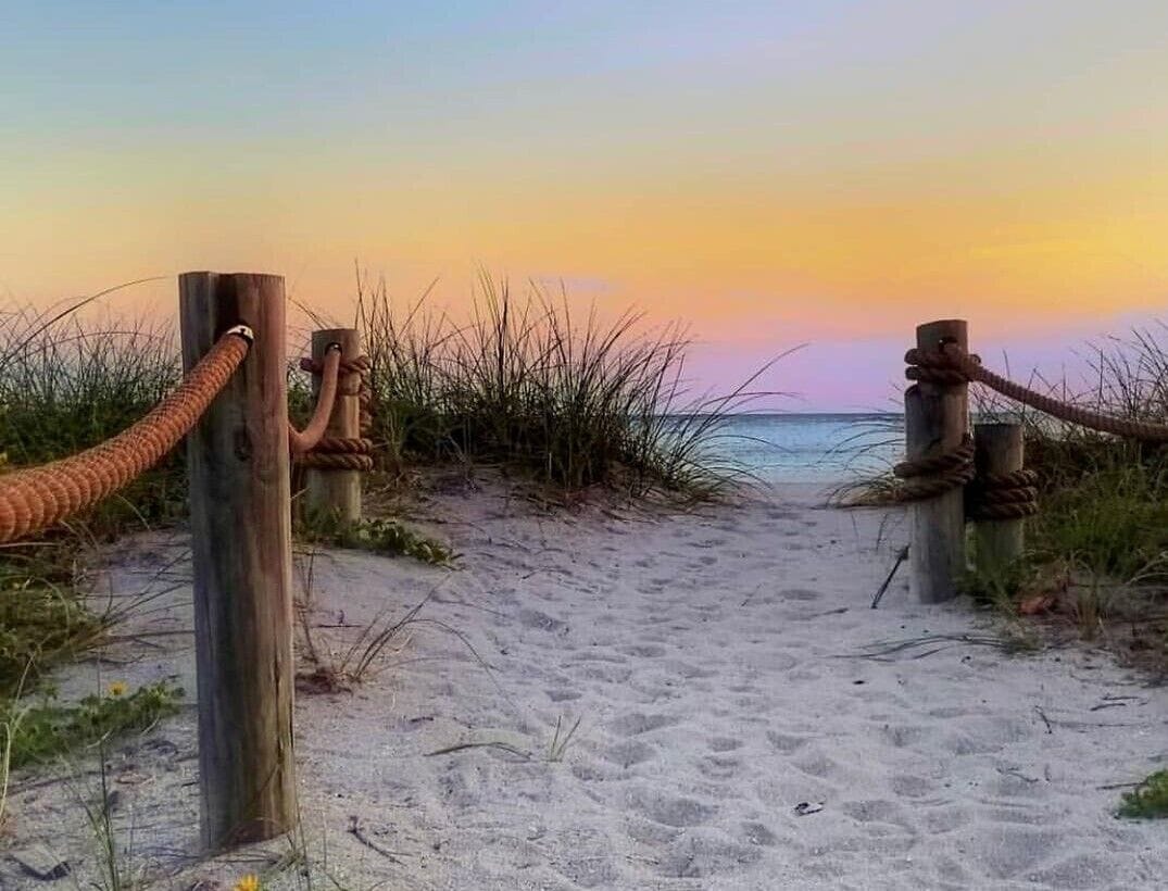 Un sentier de sable bordé de poteaux en bois et de cordes, qui mène à l’océan.