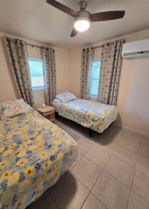 A bedroom with two beds, a ceiling fan, and an air conditioning unit. - Renovated Sarasota Cottage 4 Mi to Siesta Key  Pet Friendly  Fenced Yard (Sarasota)
