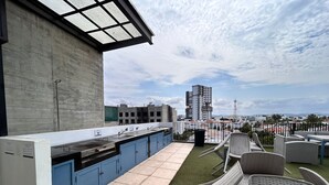 A rooftop terrace with a kitchen area, outdoor seating, and a view of the cityscape. - Condesa Apartments (Mazatlán)