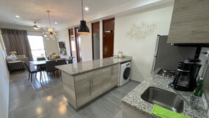 A modern kitchen with granite countertops, a built-in washer, and a coffee maker. - Condesa Apartments (Mazatlán)