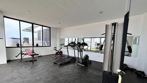 A modern gym with various exercise equipment, large windows, and a clean, spacious layout. - Condesa Apartments (Mazatlán)