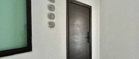 Un pasillo con una puerta oscura, un ventanal con vidrio esmerilado y un letrero con número pegado a la pared.
