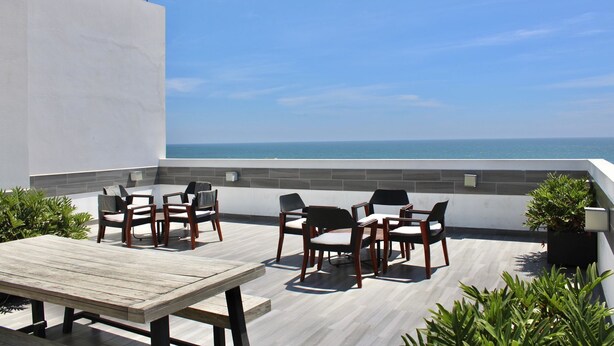 Um terraço no telhado com mesa e cadeiras de madeira, vista para o oceano e plantas em vasos.
