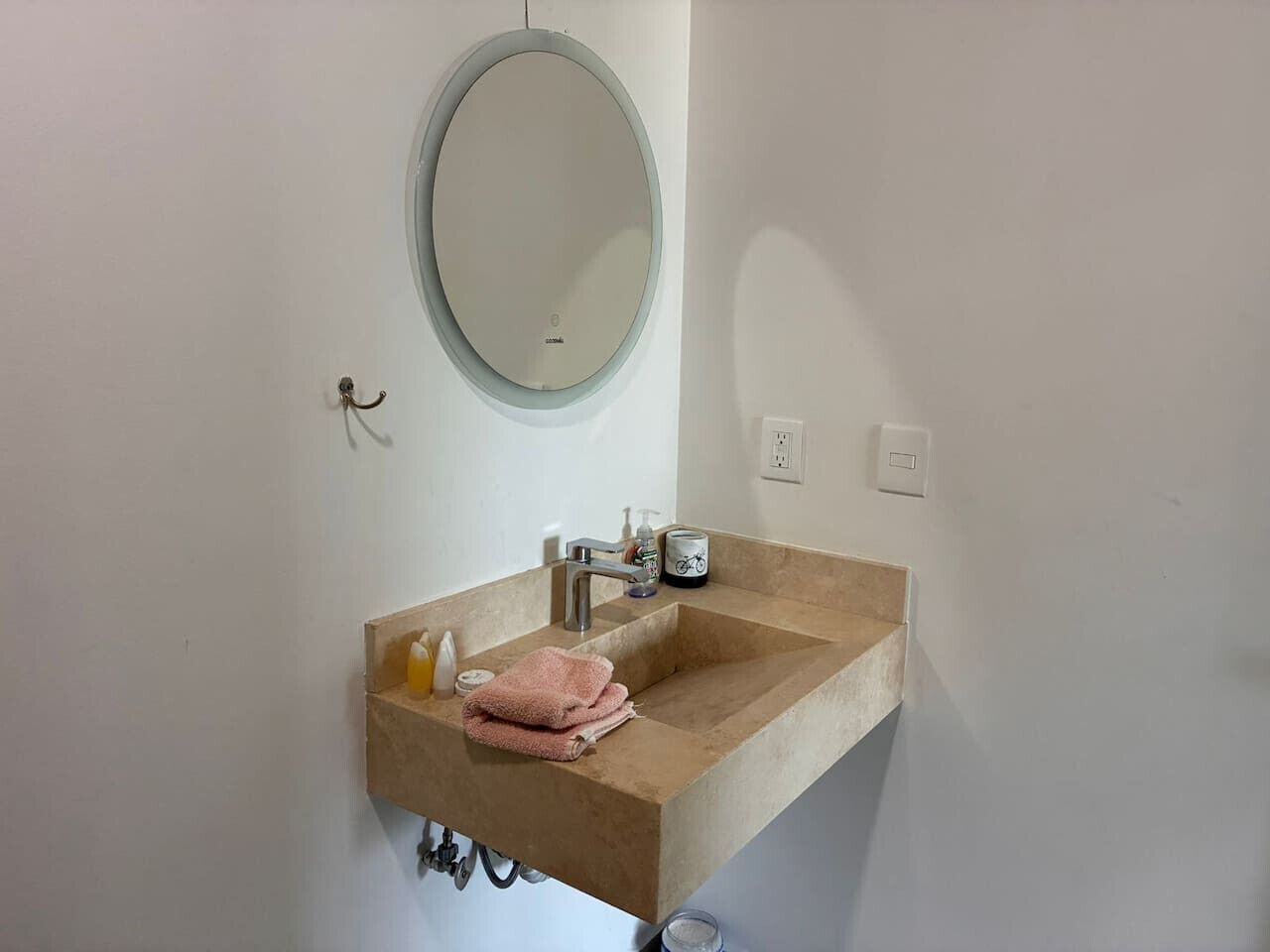 A bathroom with a beige sink, a round mirror, a towel, and a soap dispenser.