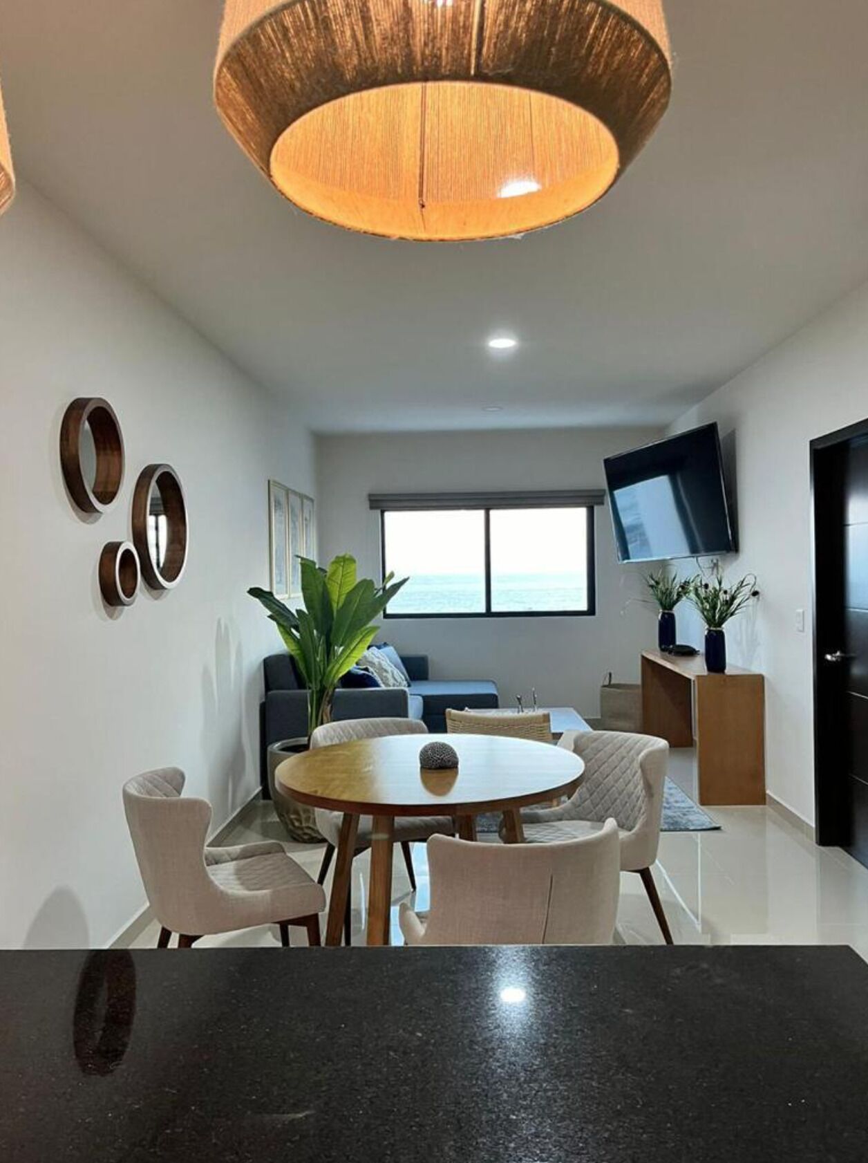 Una sala moderna con una mesa redonda de comedor, sofás, un televisor y un amplio ventanal.