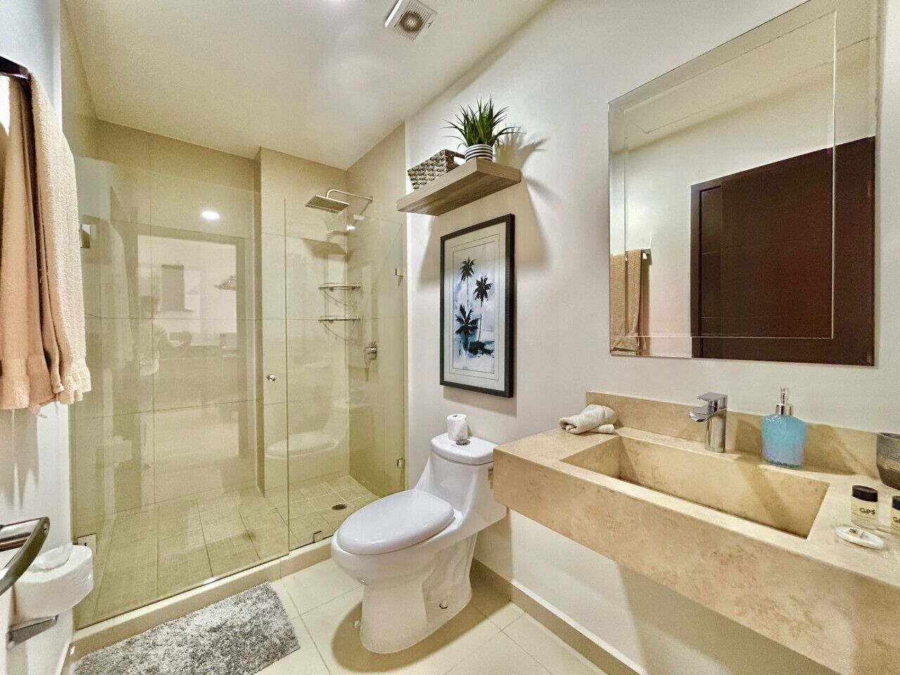 A modern bathroom with a glass-enclosed shower, a white toilet, a beige vanity, and a large mirror.