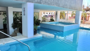 Uma piscina com borda azulejada, uma banheira de hidromassagem e uma escadaria que leva a um andar superior.