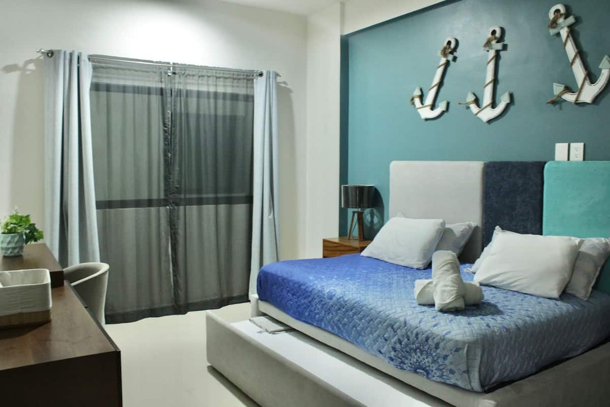 A bedroom with a bed, a desk, a chair, a lamp, and curtains.