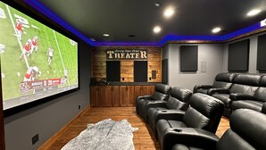 Une salle de cinéma privée dotée d’un grand écran, de fauteuils inclinables en cuir, d’un mur décoratif en bois et d’une enseigne indiquant « Cinéma ».