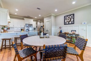 A dining area with a round table, six chairs, and a kitchen in the background.