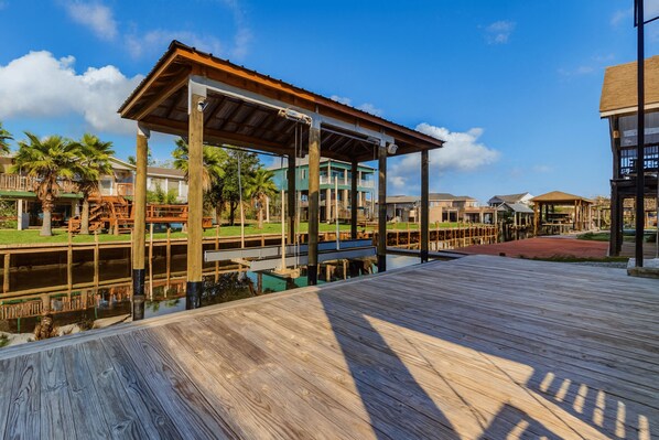 A wooden boardwalk leading to a covered pavilion with a view of a water body and buildings in the background.