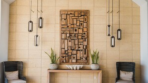 A lobby with a wooden wall art piece, two wicker chairs, a bench, and hanging pendant lights. - Gavias Grand Ocean Front (Mazatlán)