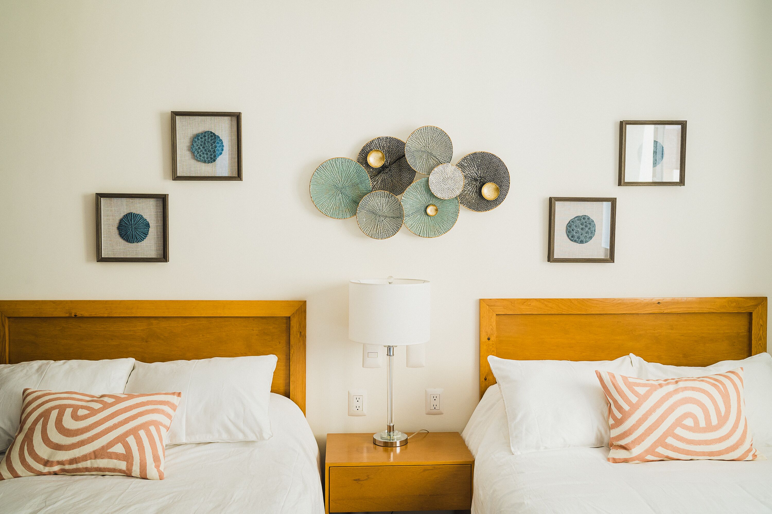 A hotel room with two beds, a nightstand with a lamp, and wall art.