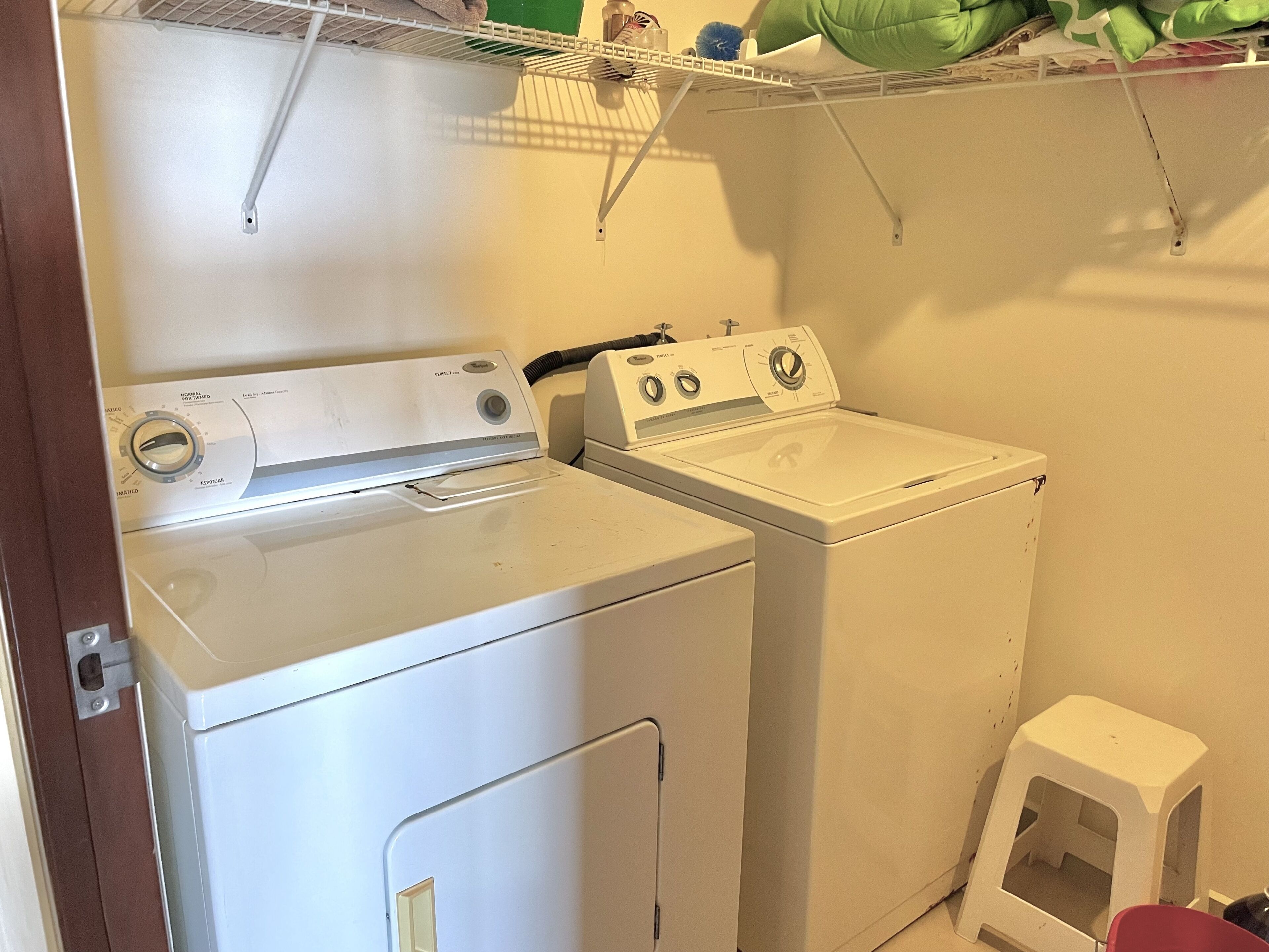 A laundry area with a front-loading washer and dryer, a small stool, and a shelf above the dryer.