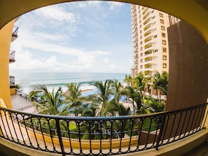 Enjoy breathtaking views of the ocean from this resort's balcony overlooking a pool area surrounded by palm trees.