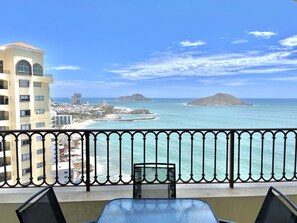 A balcony with a view of the ocean, buildings, and a distant island.