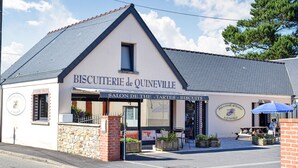A bakery named 'BISCUITERIE de QUINEVILLE' with a signboard and outdoor seating area.