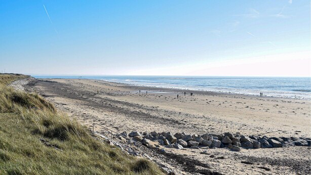 A beach with a rocky shoreline, clear skies, and a calm sea.