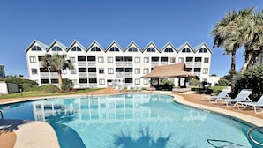 A swimming pool with lounge chairs and a building with multiple balconies in the background. - What if I told you…You CAN afford Paradise! Make the Call today! 🤙 (Gulf Shores)
