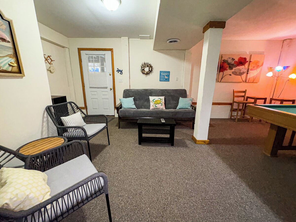 A living room with a sofa, two chairs, a coffee table, and a pool table.