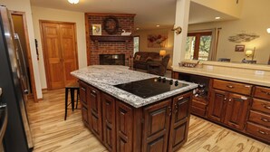 A kitchen with a central island, wooden cabinets, a built-in stove, and a brick fireplace.