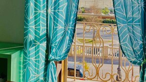 Une fenêtre ornée de rideaux à motifs géométriques, une vue sur une plage et une rambarde en métal.