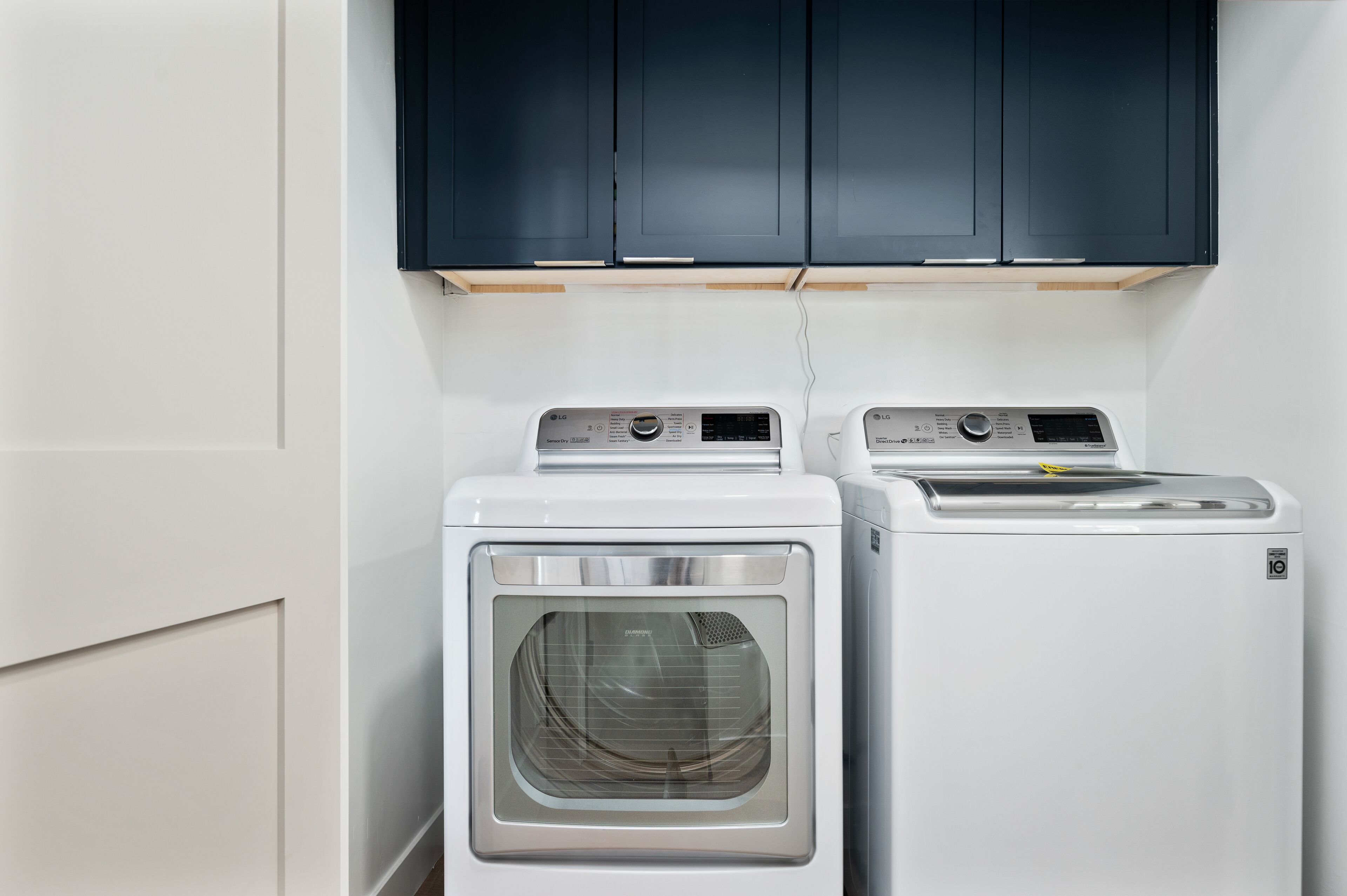 A laundry area with two front-loading washing machines and dark cabinets above.
