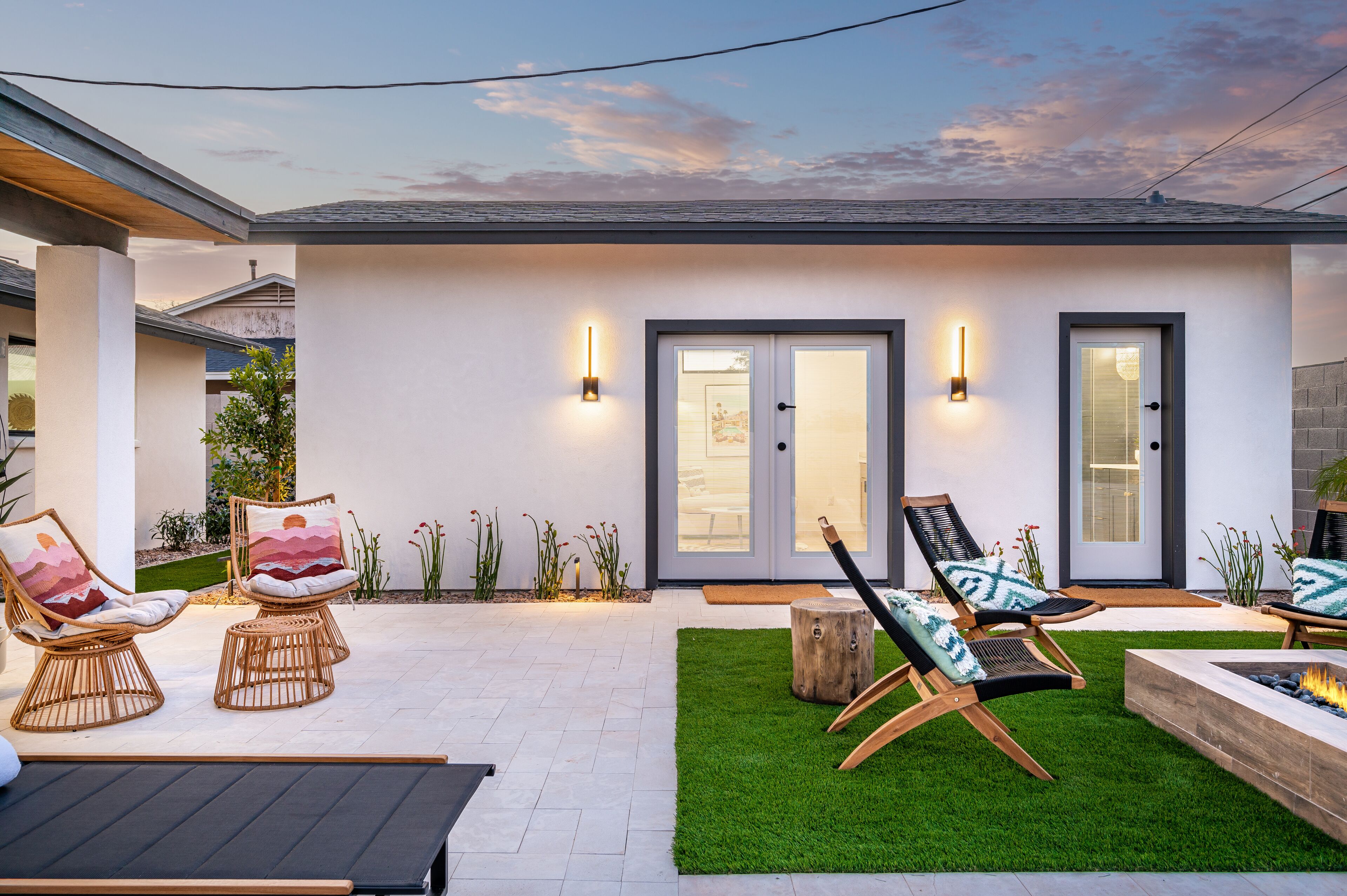 A modern outdoor patio with wicker chairs, a fire pit, and a well-maintained lawn.