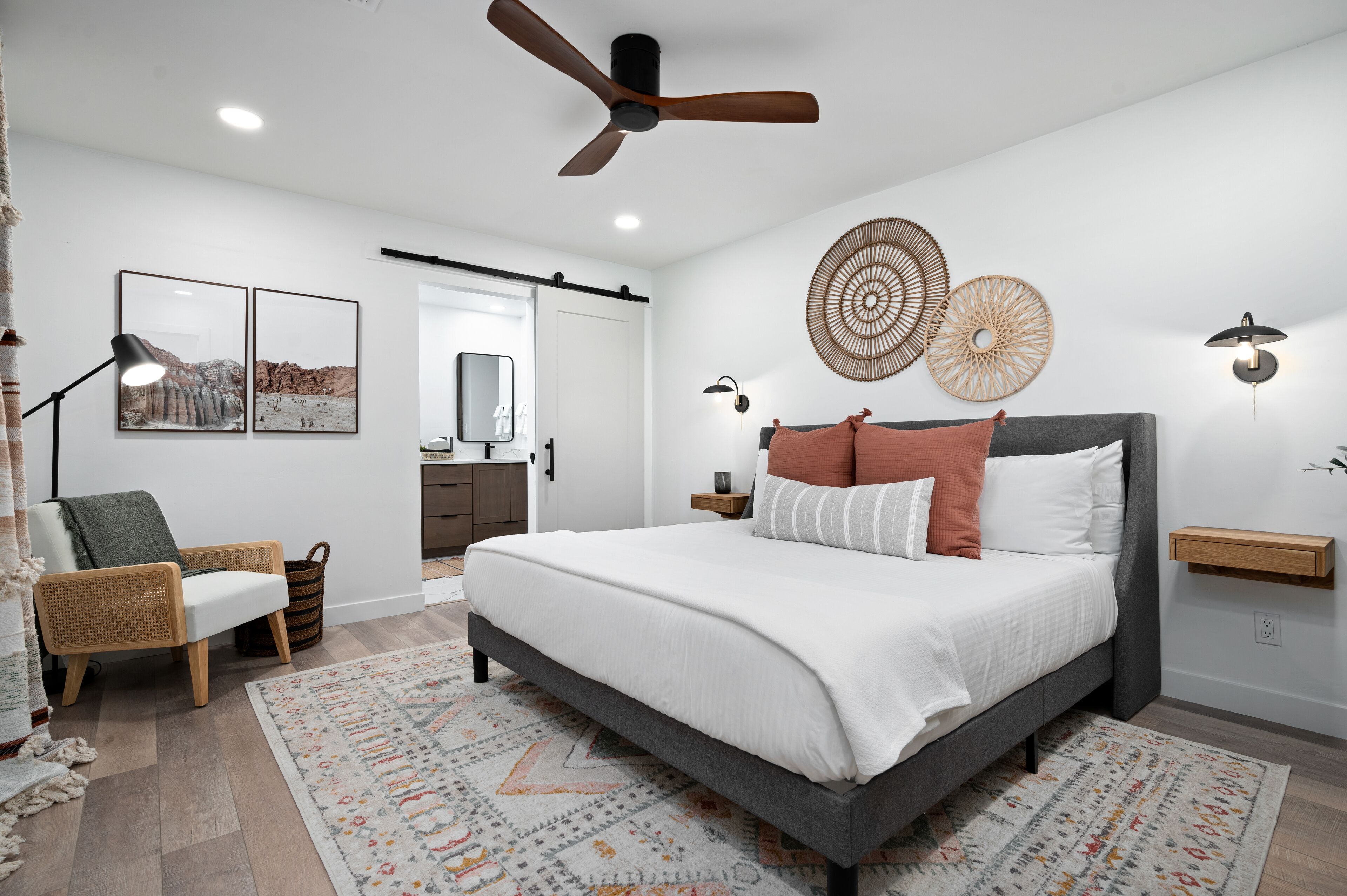 A modern bedroom with a large bed, a ceiling fan, wall art, and a bedside table.