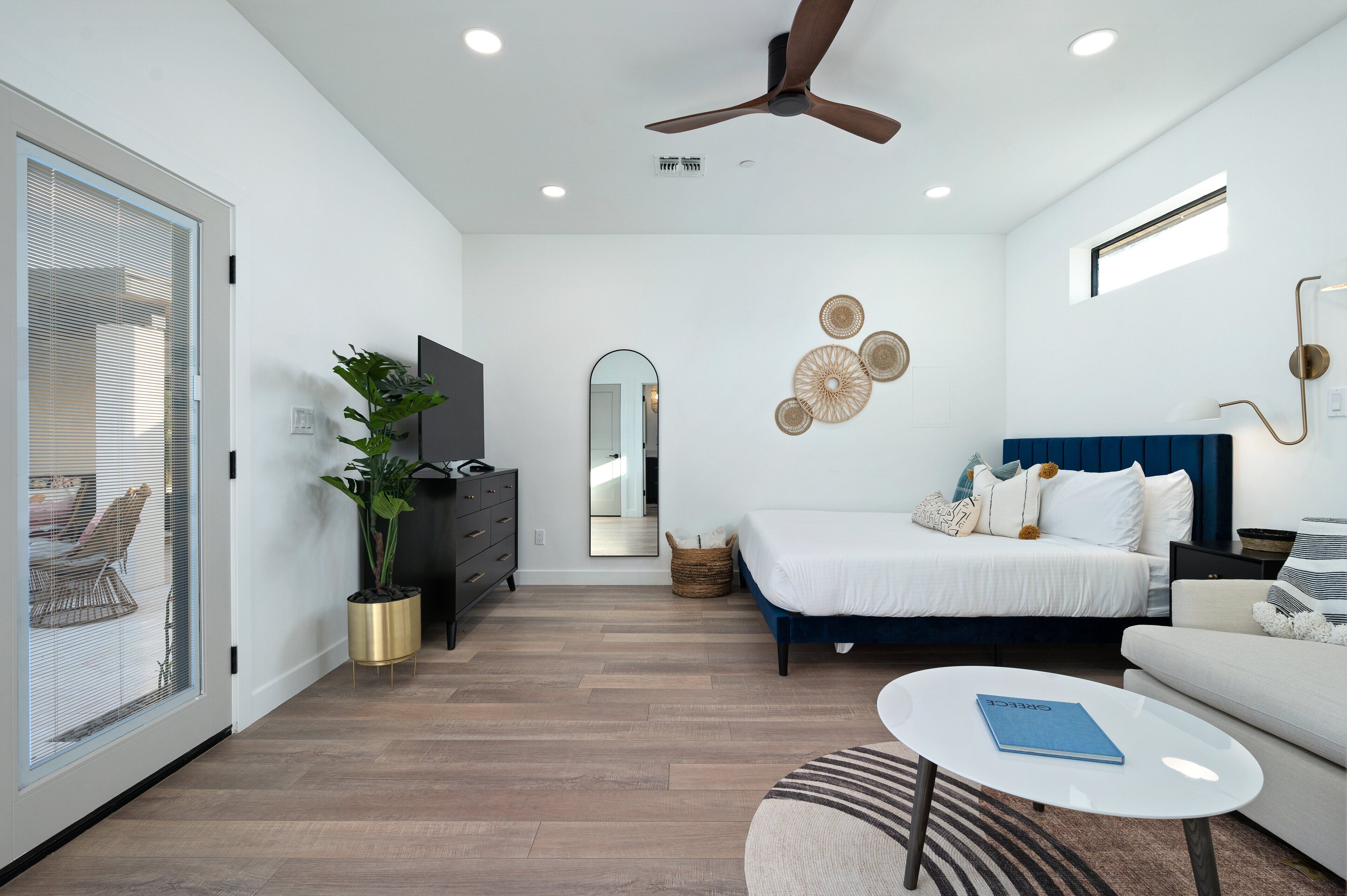 A modern bedroom with a bed, a ceiling fan, a TV, and a window with blinds.