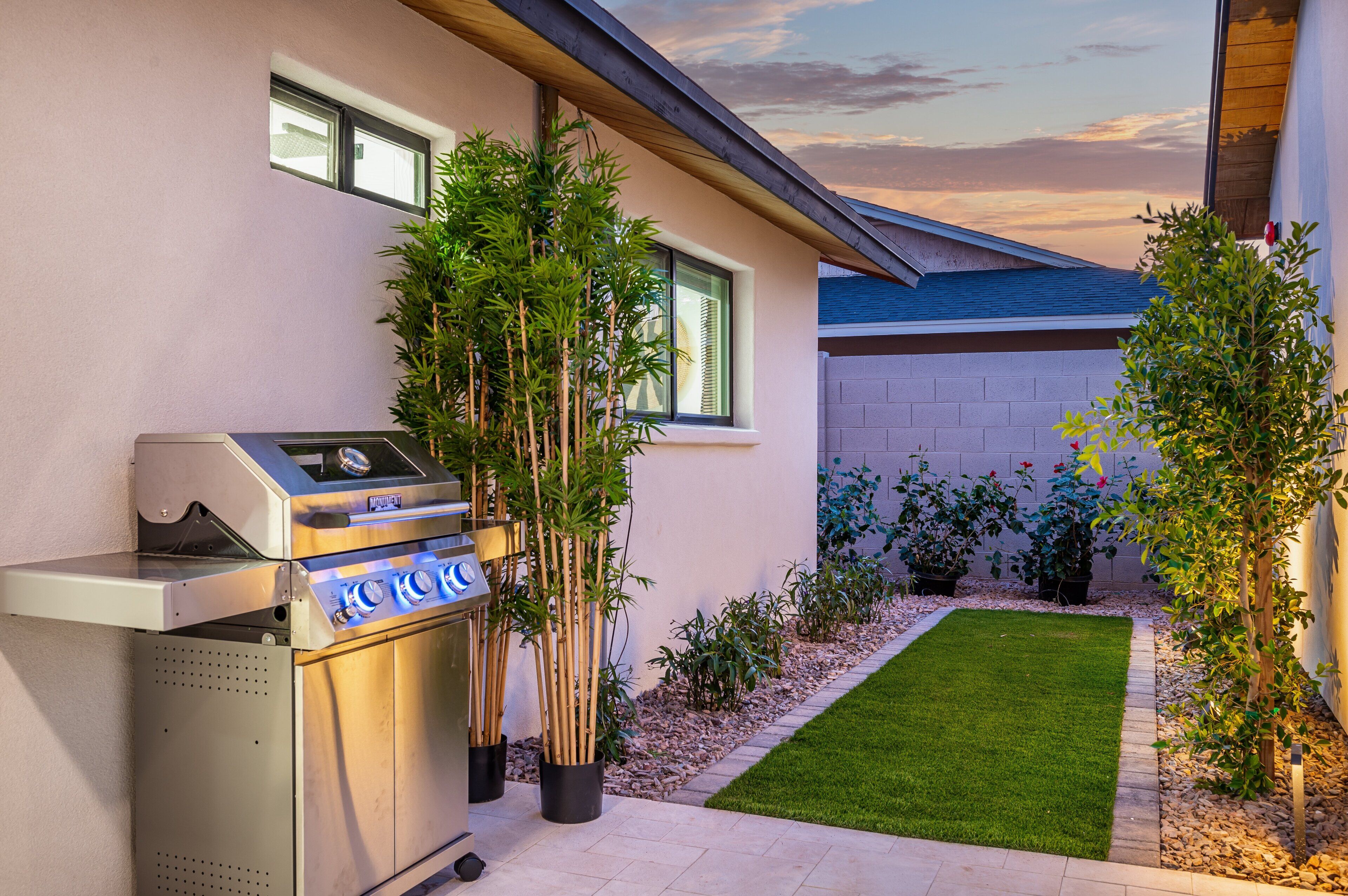 A modern house with a barbecue grill, a small lawn, and various potted plants.