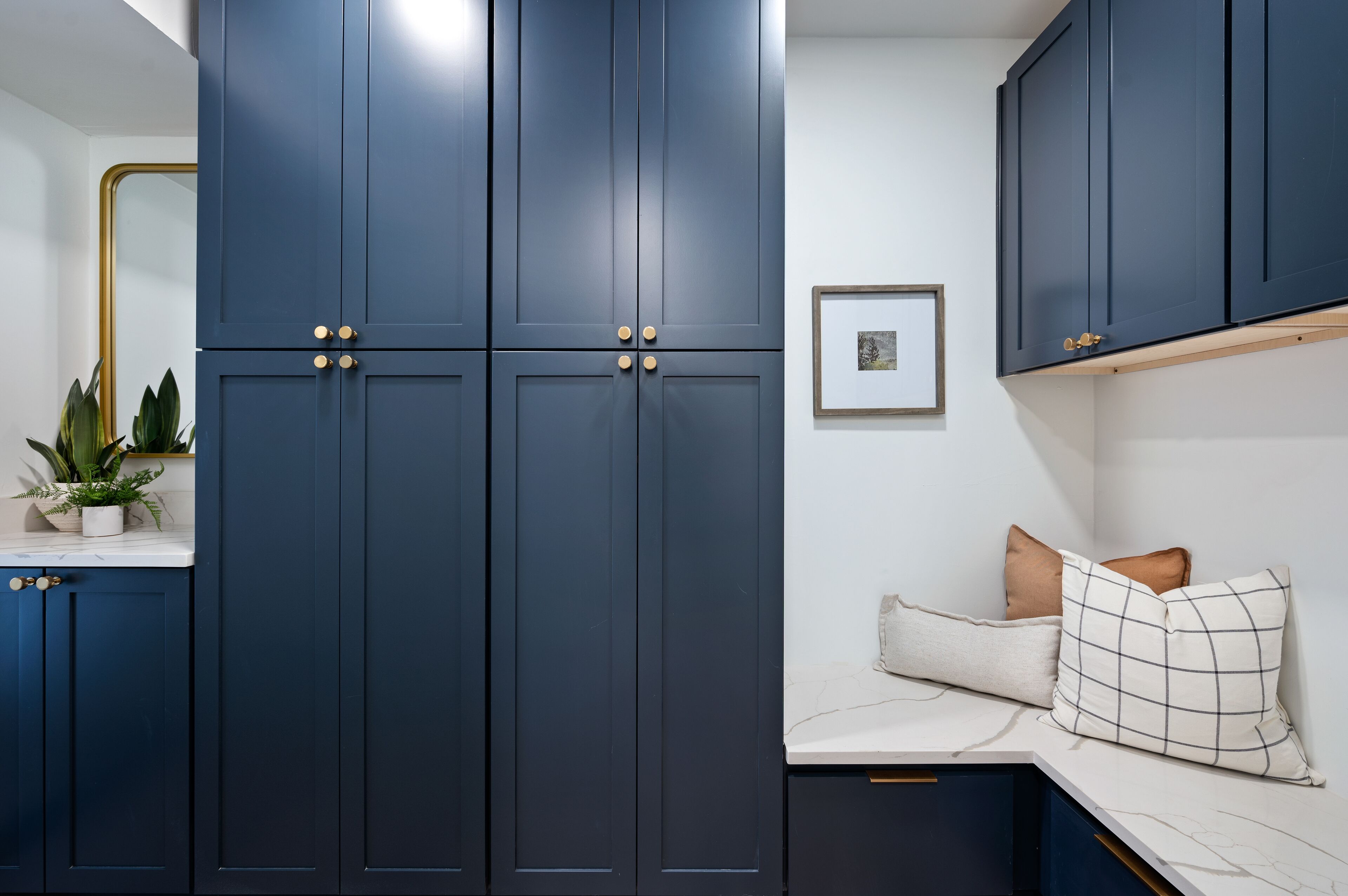 A modern kitchen with dark blue cabinets, a marble countertop, and a built-in bench with cushions.