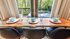 A dining table set with plates, bowls, cutlery, and glasses, with a view of a hot tub and trees through a window. - Near Dollywood | Hot Tub, Fire Pit & Games (Sevierville)
