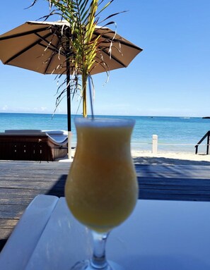 Ein Getränk in einem Glas auf einem Tisch, mit Blick auf den Strand und einer Palme im Hintergrund.
