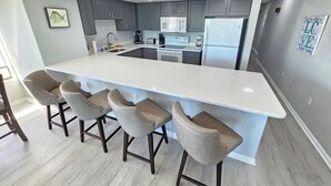 A modern kitchen with a large island, bar stools, and built-in appliances. - Beautiful Oceanfront Top-Floor Condo, Pool, Beach View, (North Myrtle Beach)