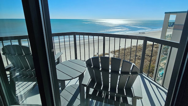 A balcony with a view of the ocean, featuring a table and chairs. - Beautiful Oceanfront Top-Floor Condo, Pool, Beach View, (North Myrtle Beach)