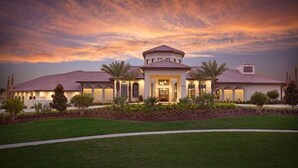 Una casa grande de dos pisos con una entrada central, rodeada de un césped cuidado y palmeras.