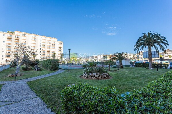 A residential area with a paved walkway, a small garden with rocks and plants, and a tall building in the background.