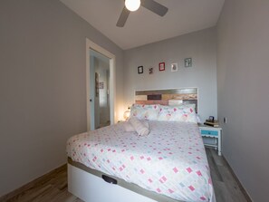 Ein Schlafzimmer mit einem Bett, Deckenventilator, Nachttisch mit Lampe und einem Beistelltisch mit Büchern.