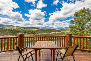 A wooden deck with a table and chairs overlooking a lake and mountains.