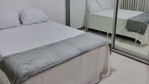A modern bedroom with a large bed, a sliding glass door leading to a balcony, and a clean, tiled floor.