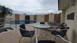 An outdoor pool area with lounge chairs and a table, surrounded by a low wall and a barbed wire fence.