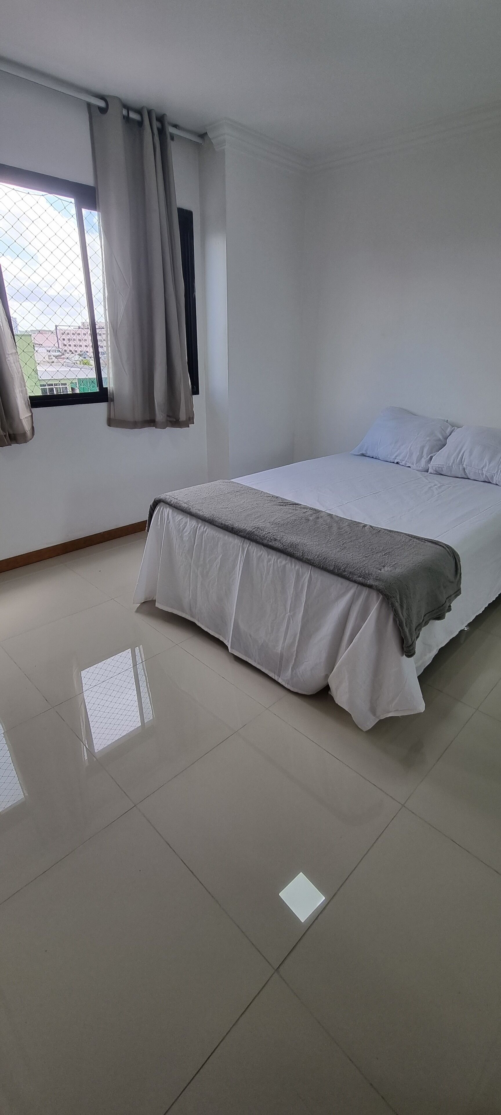 Un dormitorio con una cama, una ventana con cortinas y un suelo de baldosas.