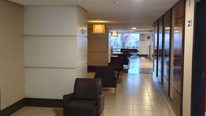 A hotel lobby with a long corridor, seating area with chairs, a coffee table, and a reception desk in the background.
