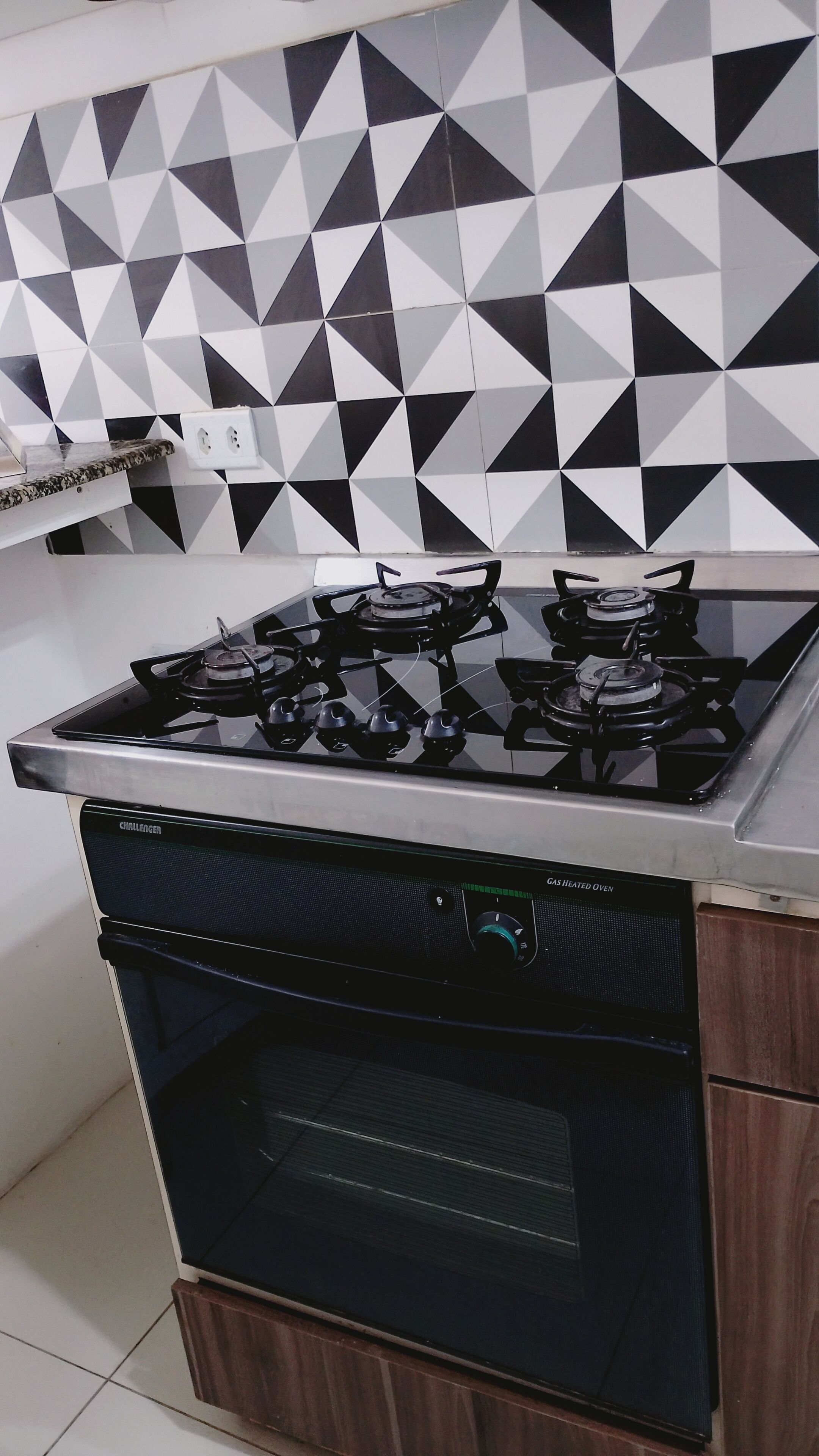 Et køkken med gaskomfur, ovn og en backsplash med geometrisk mønster.