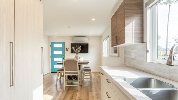 Una cocina moderna con suelo de madera, un comedor con puerta azul y un amplio ventanal con vistas.