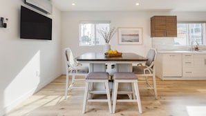 Una cocina moderna con comedor, que incluye una mesa grande, sillas blancas y un mueble de madera.