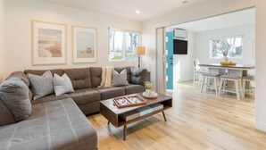 Una sala de estar moderna con un sofá modular, una mesa de centro con juegos de mesa y un comedor con una mesa y sillas.