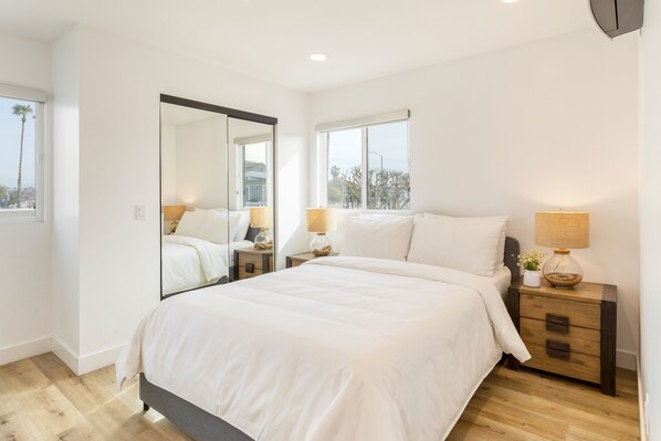 A modern bedroom with a large bed, a nightstand with a lamp, and a mirror.